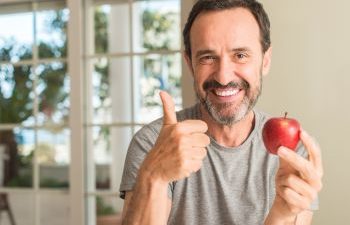 Smiling mature man eating an apple and showing his thumb up.