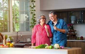 Happy senior Indian asian couple husband and wife have fun sing in kitchen appliances cooking together at home.
