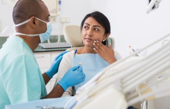 Woman patient talking to male dentist and complaining of toothache at dental clinic office